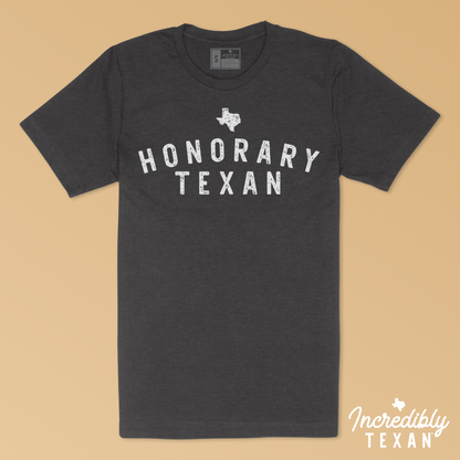 A dark gray short sleeve t-shirt with "HONORARY TEXAN" printed in white with the state of Texas above.